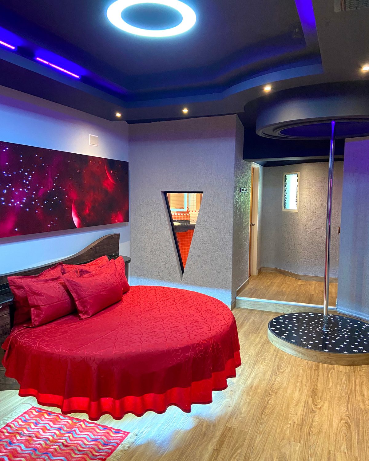 The Moon: cama redonda roja, aro de luz en el techo y tubo con tarima iluminada