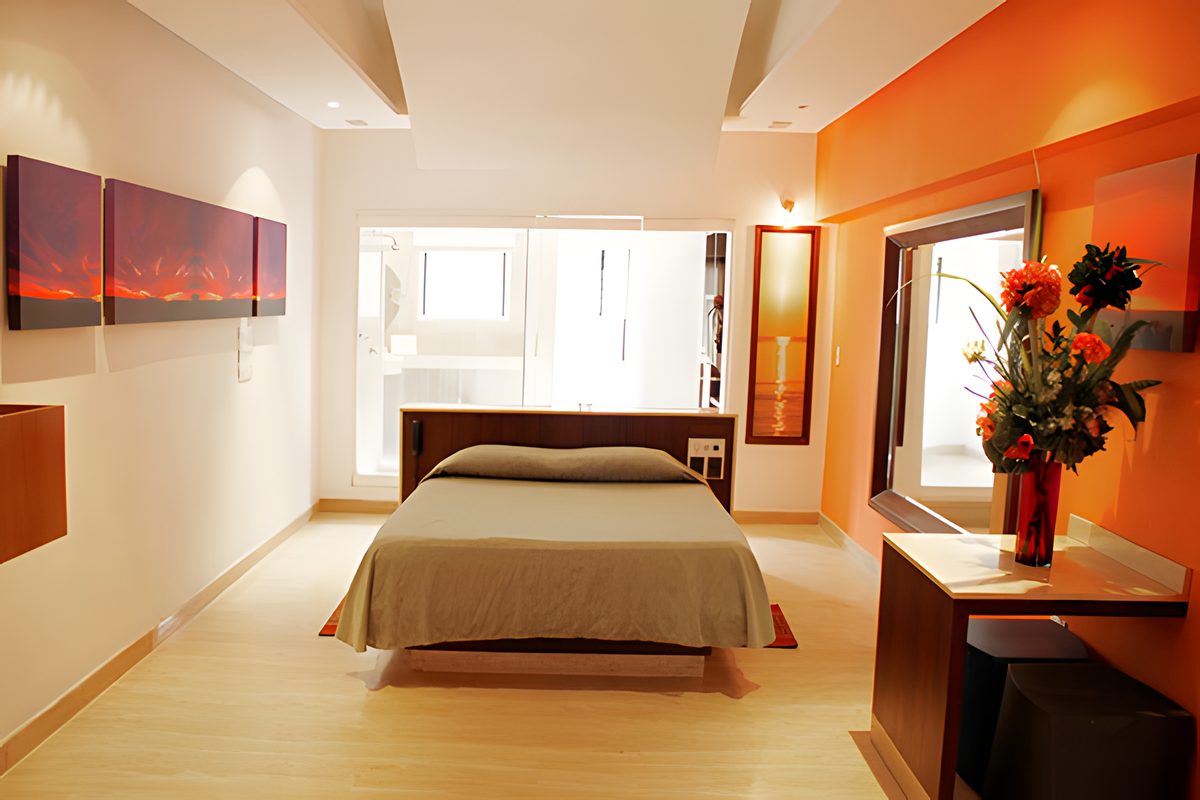 Lounge: cama central, pared naranja, cuadros y escritorio con flores